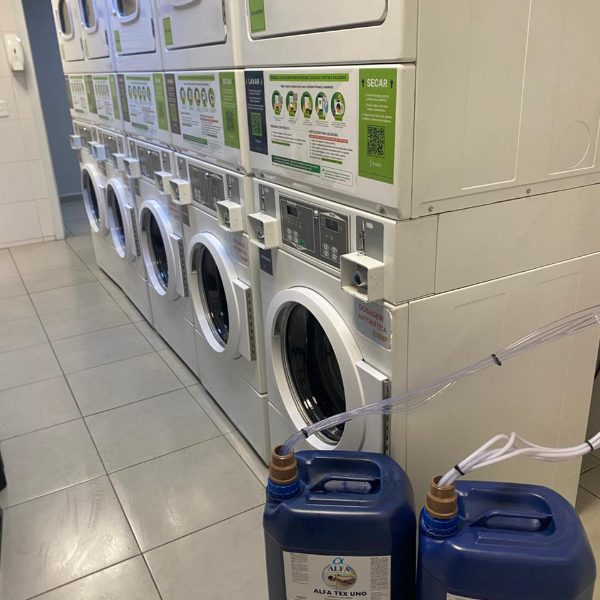 Bombonas Alfa Tex Uno e Alfa Soft Uno alimentando a fila de lavadoras de uma lavanderia de autosservico atendida pela Protego